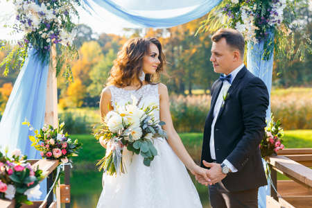 Elegant curly bride and happy groom outdoors on the background the lake. Creative stylish wedding ceremonyの写真素材