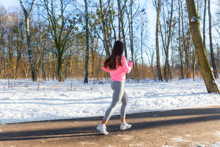 Young girl goes in for sports in winter park. Jogging training.の写真素材