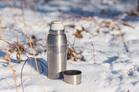 open thermos with hot tea in the snow in the winterの写真素材