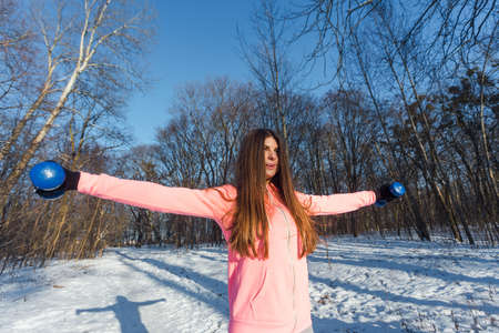Active young woman performs an exercise with a dumbbells in winter parkの写真素材