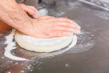 Cook forms a dough pizza base. Hands closeup.