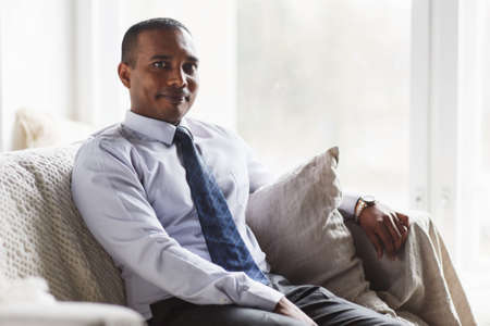 Image of young African man sitting in room and looking at cameraの写真素材