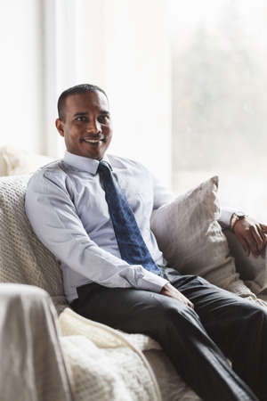 Image of young African man sitting in room and looking at cameraの写真素材