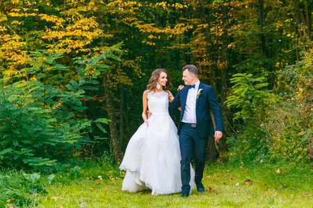 Elegant curly bride and stylish groom walking in beautiful summer parkの写真素材