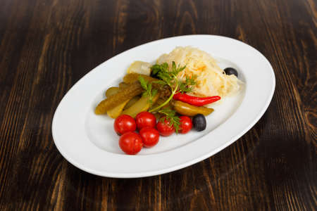 Pickled vegetables. Appetizer of tomatoes, cucumbers, cabbage and pepper close-up in white plate on the wooden tableの写真素材