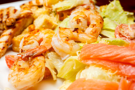Background from salad of romaine lettuce with prawns, smocked salmon, croutons, grilled chicken, cherry tomatoes with caesar dressing and grated parmesan on rectangular dishの写真素材