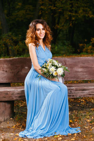 Beautiful young bridesmaid sitting in the park on the wedding dayの写真素材