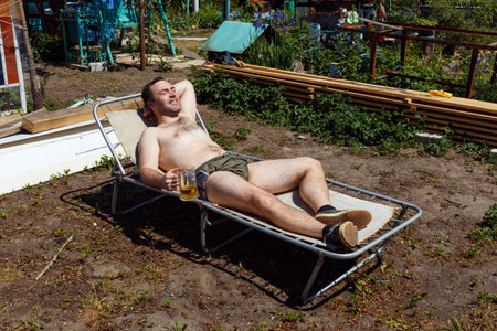 A man sunbathes on a cot and drink beer in the yard of a country houseの写真素材