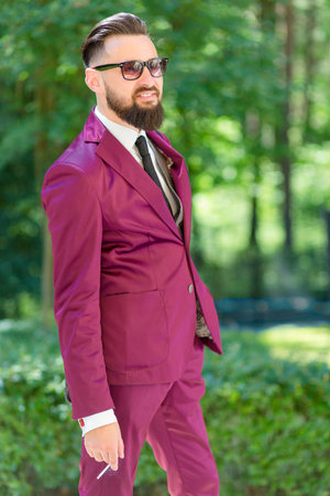 A young handsome businessman smoking on the background of the Parkの写真素材