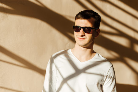 A young man in white wear posing against the wall