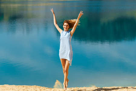 Young woman in a blue dress jumping on the beach by the ocean. Happy vacationの写真素材