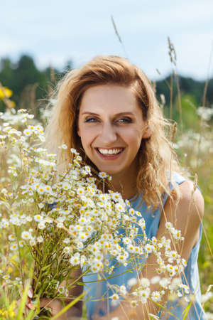 Beautiful young woman on the daisy flowers field look in camera and smilingの写真素材