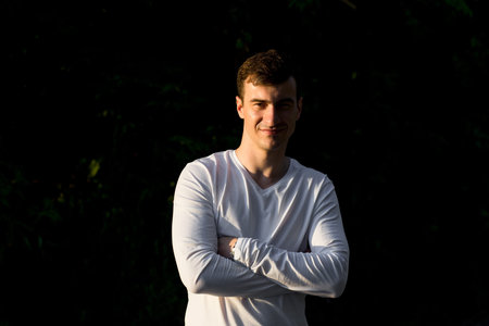 A young man in white wear posing on dark background