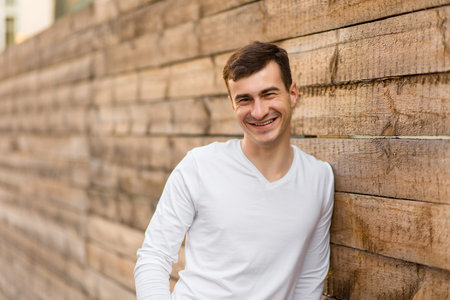 A young man in white wear posing near by wooden wallの写真素材