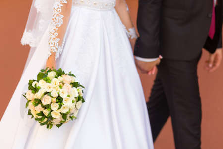 Groom holds bride's hand walking with her on the streetの写真素材