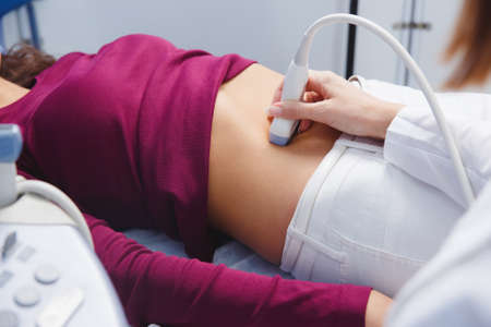 female doctor operating ultrasound scanner examining belly of her female patientの写真素材