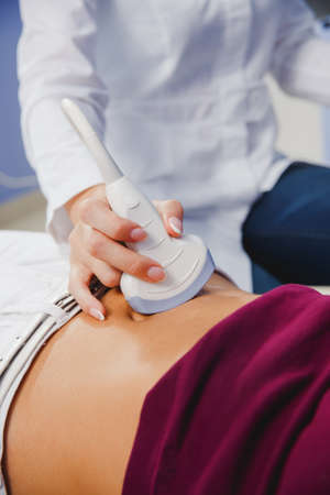 female doctor operating ultrasound scanner examining belly of her female patientの写真素材