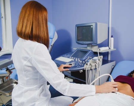 female doctor operating ultrasound scanner examining belly of her female patientの写真素材