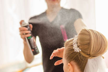 Stylist helping bride prepare for wedding using hairsprayの写真素材