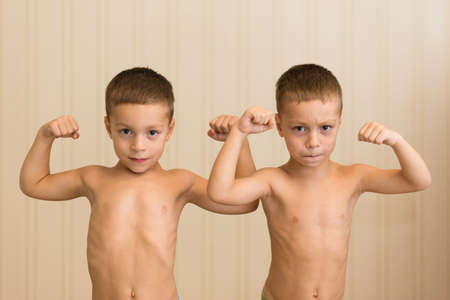 Two boy twins demonstrate the muscles on their handsの写真素材