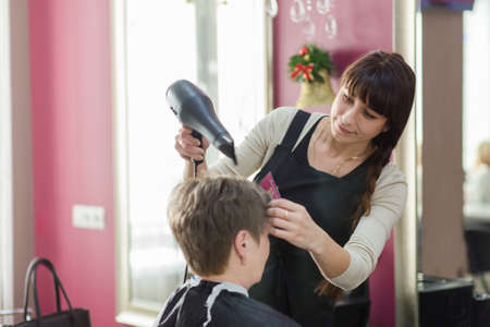 Grodno, Belarus - December 13, 2017: A hairdresser drying hair of adult woman in beauty salonのeditorial素材