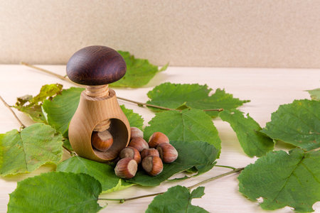Wooden mushroom shape nutcracker and hazelnuts on wooden table. Screw type nut cracker with...