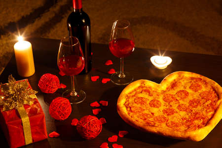 Heart shaped italian pizza with pepperoni and mozzarella and red wine bottle decorated with hearts and flowers. Valentines day stll life.の写真素材