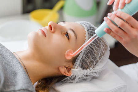 Violet ray treatment on face at the beautician. A violet ray is an antique medical appliance used during the early 20th century in the obsolete medical therapy called electrotherapy.の写真素材