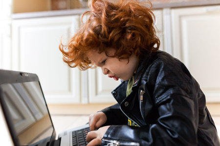 Little redhead boy uses a laptop while sitting on the floor at homeの写真素材