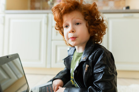 Little redhead boy uses a laptop while sitting on the floor at homeの写真素材