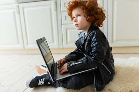 Little redhead boy uses a laptop while sitting on the floor at homeの写真素材
