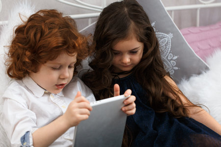 A boy and a girl lie on the bed and play with a tablet computer.の写真素材