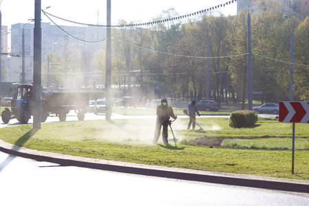 Workers mow grass on lawns in the city early in the morningの写真素材