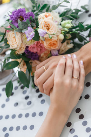 Close-up of wedding hands with rings and bouquet lie on the tableの写真素材