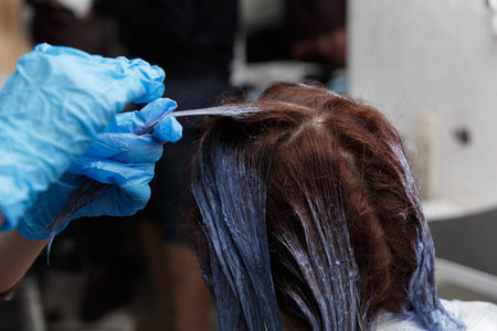 Hairdresser salon. Hair colouring in process. Woman dyeing hairs in dark color.