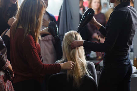 Two masters at the same time dried with hair dryers hair blonde model in beauty salon. Rear view.の写真素材