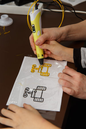 Close up of 3D printing pen being used by kid. The teacher helps to use the device. Technology...