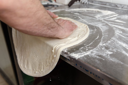 Cook forms a dough pizza base. Hands closeup.