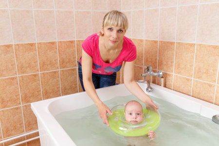 Newborn baby swimming in the bath or bathtub. Mother help him swim. Mom teaches him to swim and...