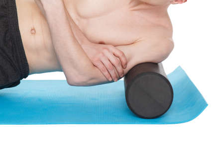 Handsome man shows exercises, using a foam roller for a myofascial release massage on exercise mat in studio. Isolated on white.の写真素材