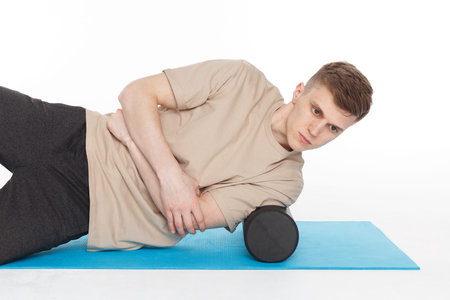 Handsome man shows exercises using a foam roller for a myofascial release massage of trigger points....