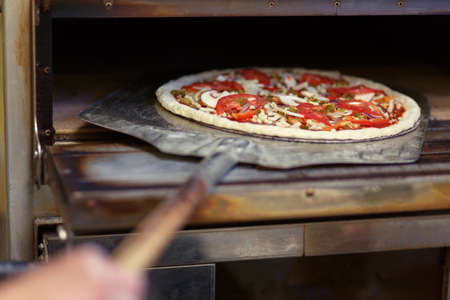 Food concept. Preparing traditional italian pizza. Chef holds long iron shovel for pizza, baking dough with pasta and cheese in a professional oven. の写真素材