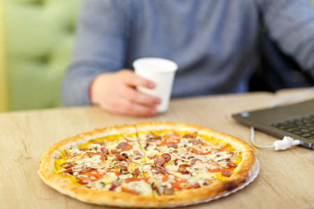 Business or study concept. Pizza stands on a table in a cafe. A person combines eating and working on a computer.の写真素材