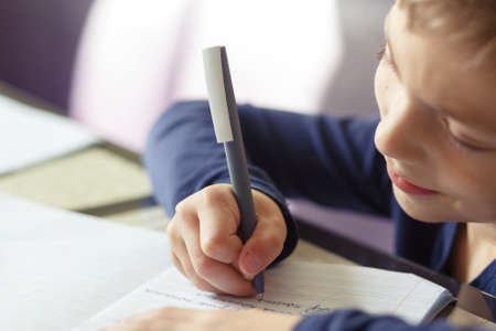Schooler is engaged in home schooling. The boy sits at a table, writes, draws and learns online on the Internet. Quarantine due to the coronavirus pandemic, covid-19の写真素材