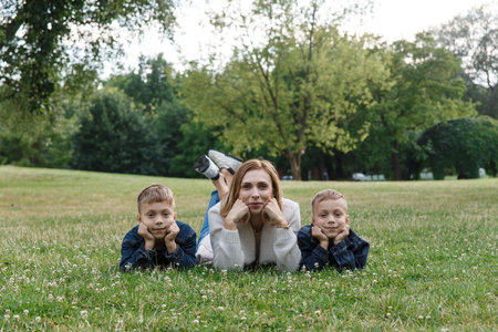Family, leisure and people concept - happy mother and two sons laying on meadow in summer park