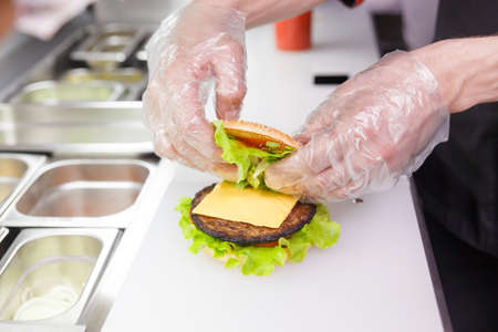 Cook adding a second half of the burger. Preparing burger in restaurant. Hands of the cook in disposable gloves based on hygiene requirements.の写真素材