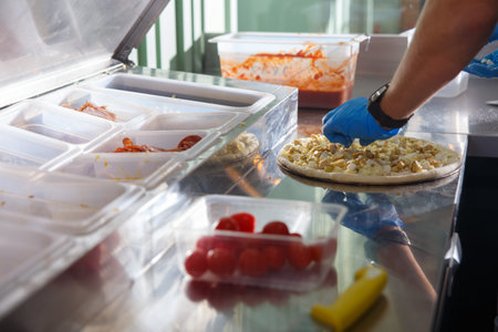 A man in a cafe is preparing pizza. The ingredients for packaging are in containers and signed.の写真素材
