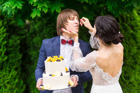 Newlyweds and bridesmaids have fun and eat wedding cake together in the fresh air on wedding banquet.の写真素材