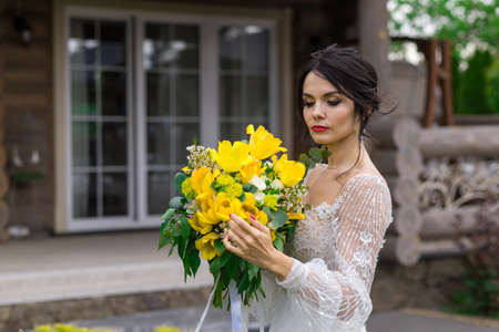 The charming bride keeps a wedding bouquet and posing on yardの写真素材