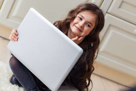 Small cute brunette caucasian baby sitting on floor on light artificial animal skin and watching cartoons on laptop with great interest.の写真素材